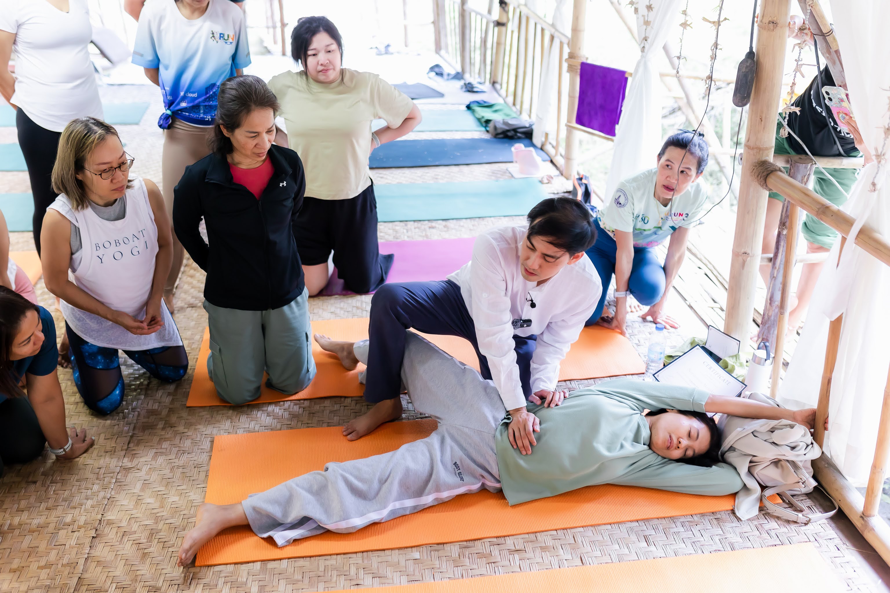 ภาพการสาธิตปรับท่าแบบ hands-on · กลุ่มผู้เรียนล้อมรอบนักเรียนที่นอนรับการปรับ